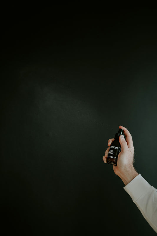 Hand spraying dark liquid from bottle against dark background